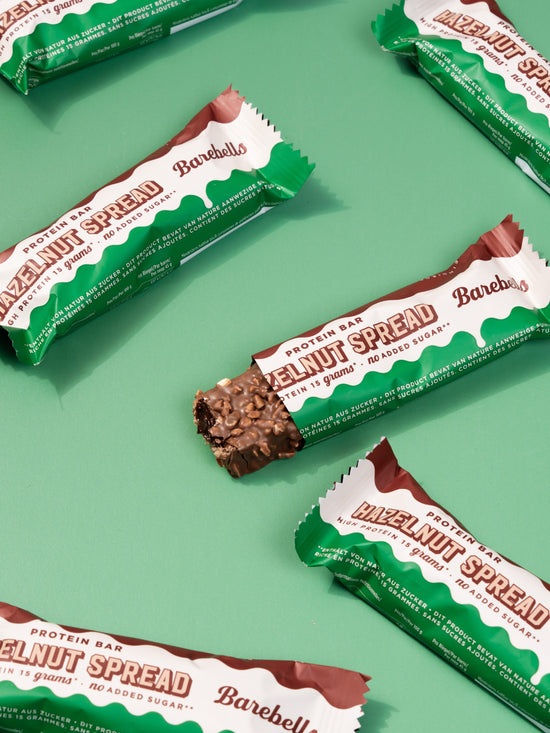 Five Barebells Hazelnut Spread protein bars with white and green wrappers arranged diagonally on mint green background