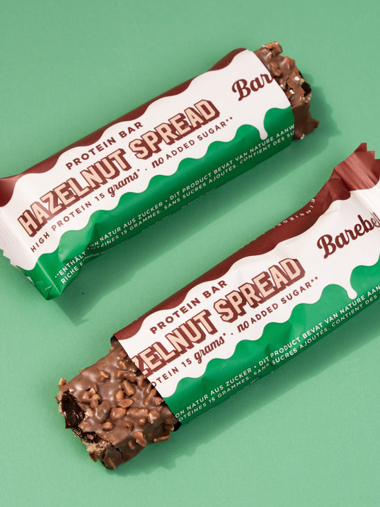 Two Barebells Hazelnut Spread bars with white and green packaging on mint background, one showing unwrapped chocolate end